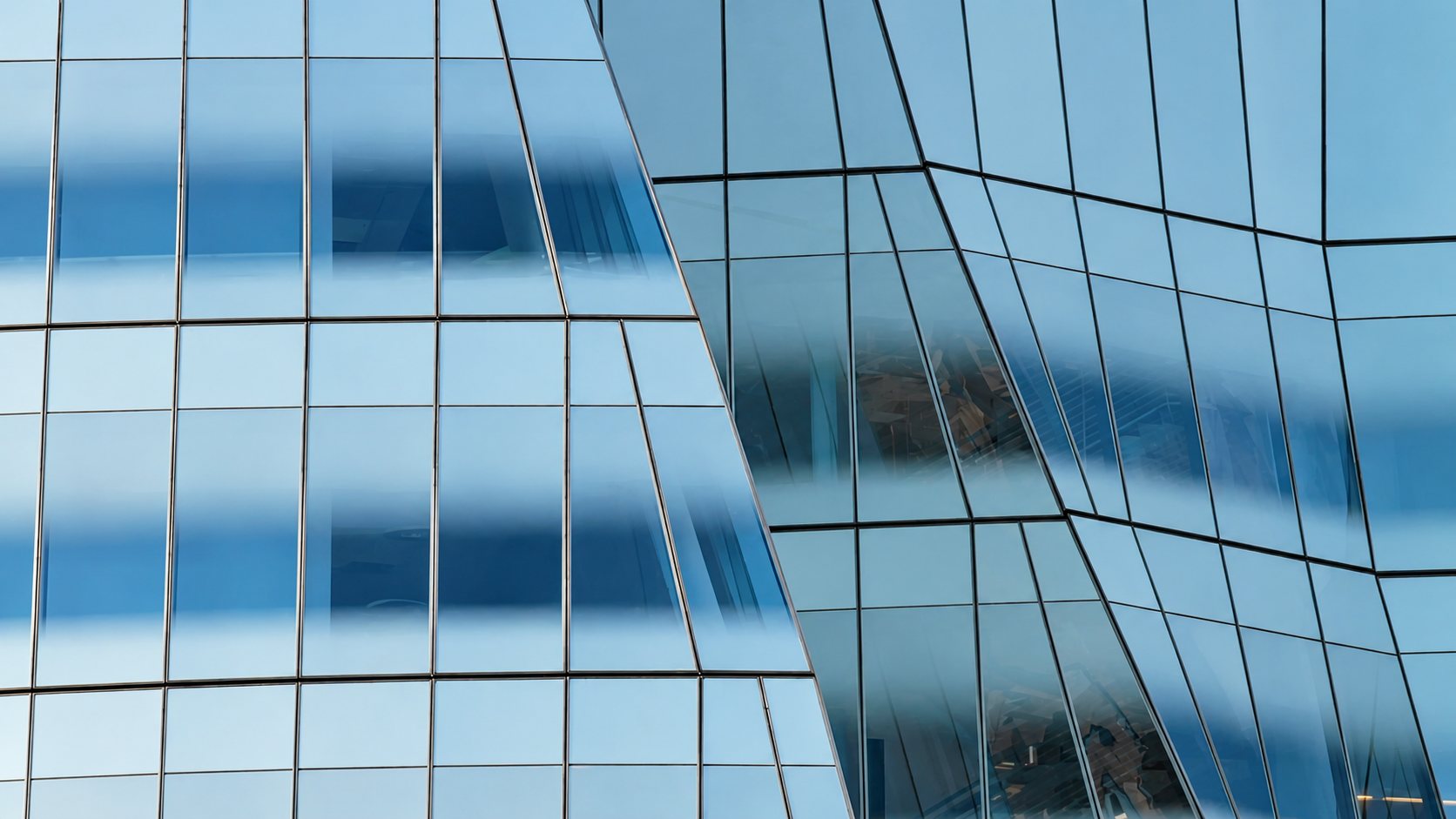 Gros plan sur la façade vitrée d'un bâtiment contemporain aux panneaux de verre inclinés qui reflètent le ciel bleu.